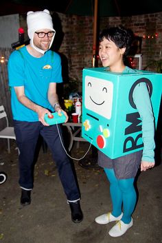 two people dressed up in costumes and one is holding a wii game controller while the other holds a box