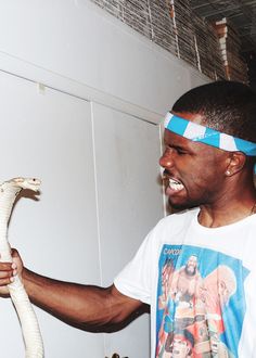 a man holding a snake in his right hand and wearing a bandana around his head