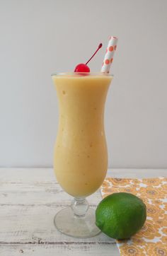 a smoothie in a glass with a straw and a cherry on the rim next to a lime