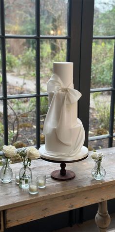 a three tiered white wedding cake sitting on top of a wooden table next to vases