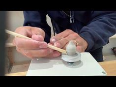 a person is working on something with a wooden stick and glue in their hands while sitting at a table