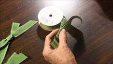 someone is holding a green ribbon on top of a wooden table with scissors and tape