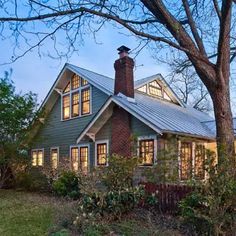 the house is surrounded by trees and bushes, with lights shining on it's windows