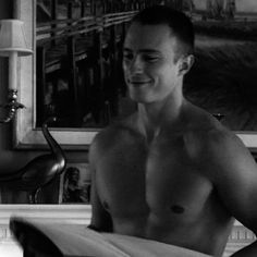 black and white photograph of a shirtless man holding a towel in front of a sink