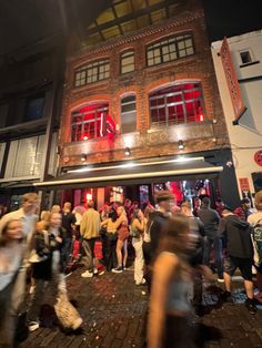 a group of people standing in front of a brick building at night with red lights