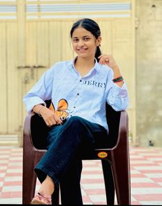 a woman sitting on top of a wooden chair in front of a building with a butterfly on her shirt