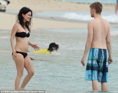 two people standing in the water on a beach with one person wearing a bathing suit