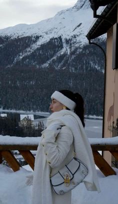 a woman is standing outside in the snow with her hand on her shoulder and looking at mountains