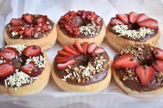 six donuts with chocolate frosting, strawberries and nuts on top in a box