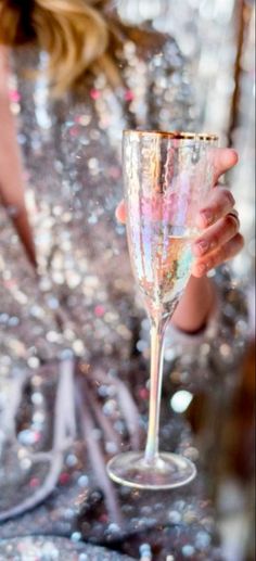 a woman is holding a wine glass in her hand while wearing a sequin dress