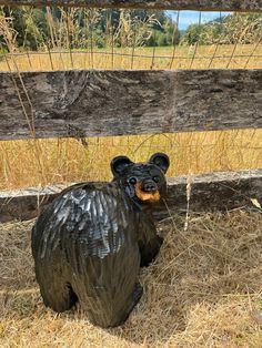 a black bear statue sitting in the grass next to a wooden fence and some dry grass