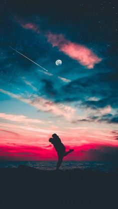 two people standing on top of a hill under a night sky with the moon in the distance