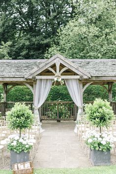 an outdoor wedding venue with chairs and flowers in the foreground, surrounded by greenery