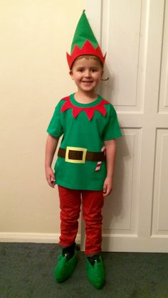 a young boy dressed up as an elf standing in front of a white door wearing green shoes