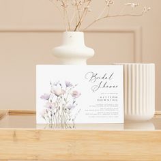 a white vase filled with flowers on top of a wooden table next to a card