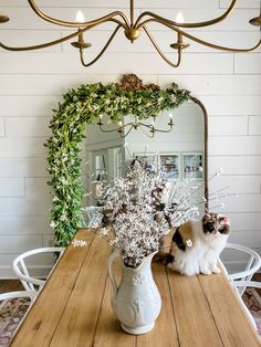 a cat sitting on top of a wooden table next to a vase filled with flowers