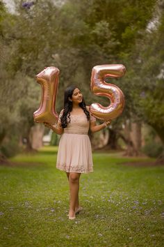 a woman in a dress is holding up some balloons that spell the number fifteen five