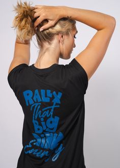 Don't just play the game. To win, you have to show up with BIG energy! This top is a soft, fashion-forward, women's muscle tee and comes with rolled cuff sleeves that add an element of style, and a high-low, raw-edge hem gives it need-now appeal. Available in Night (black). Features: Side seamed. Relaxed, draped fit. Rolled cuff. Hi low raw bottom hem.Fabrication: 65% polyester 35% viscose, 32 single, 3.7 oz. Fan Apparel Tops With Graphic Design For Sports Events, Athleisure Tops With Screen Print For Sports Events, Sporty Tops With Graphic Design, Casual Tops With Graphic Design For Sports Events, Casual Graphic Top For Sports Events, Graphic Design Fan Apparel Tops For Sports Events, Sporty Graphic Design Tops, Crew Neck Graphic Tops For Sports Events, Sporty Tops With Graphic Design For Fan Merchandise