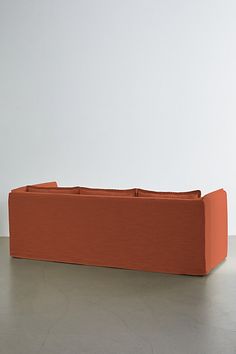 an orange couch sitting on top of a floor next to a white wall and chair