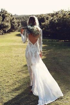 a woman in a long white dress is walking through the grass with her back to the camera