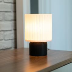 a lamp sitting on top of a wooden table next to a brick wall and window