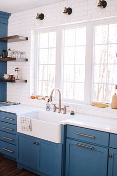 a kitchen with blue cabinets and white subway tile backsplash, stainless steel faucet, and open shelving