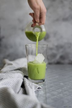 someone pouring green liquid into a glass with ice cubes on the side and a towel next to it