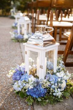 a white lantern with blue flowers and greenery on the ground at a wedding ceremony