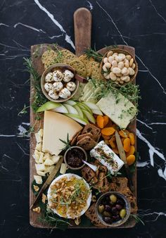 an assortment of cheeses, crackers and nuts on a platter with a wooden spoon