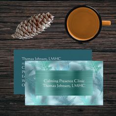 a cup of tea next to a business card on top of a wooden table with a pine cone