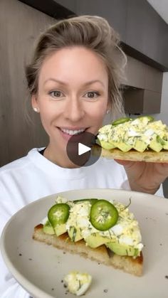 a woman holding up a piece of food with cucumbers on it and the other half eaten sandwich