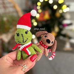 a hand holding a small crocheted stuffed dog and teddy bear in front of a christmas tree