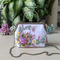 a purse with flowers painted on it sitting on a table next to some potted plants