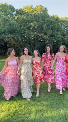 four women in dresses are standing on the grass