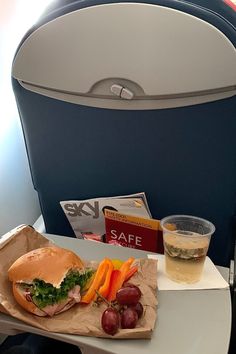 an airplane seat with a sandwich and grapes on the tray, next to a drink