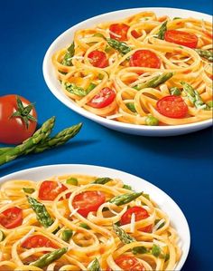 two plates of pasta with tomatoes and asparagus