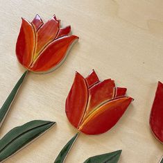 three red flowers sitting on top of a table next to each other with green leaves