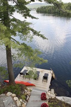 a dock with chairs on it next to the water and trees in the foreground