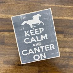 a wooden sign that says keep calm and canter on with a horse running across it