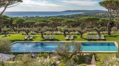 an outdoor swimming pool surrounded by trees and lawn chairs with the ocean in the background