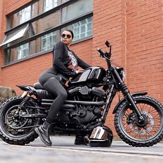 a woman sitting on top of a motorcycle in front of a brick building wearing sunglasses