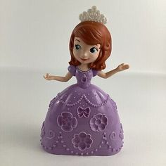 a purple princess figurine sitting on top of a white surface with her arms outstretched