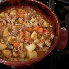 a red bowl filled with meat and vegetables on top of a stove burner next to an oven