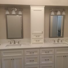 a bathroom with double sinks and two mirrors on the wall, along with white cabinets