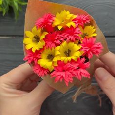 a person holding a bunch of flowers in their hand on a wooden table next to a potted plant