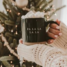 a woman holding a black coffee mug with the words fa la la la on it