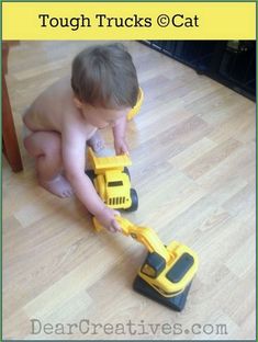 a toddler playing with a toy truck on the floor in front of a cat