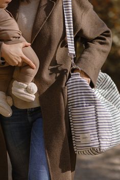 a woman holding a baby in her arms while wearing a coat and striped shirt is walking down the street