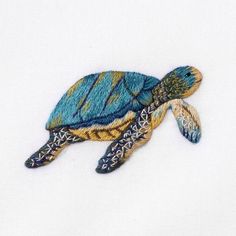 a blue and yellow turtle embroidered onto a white shirt with an intricate design on it