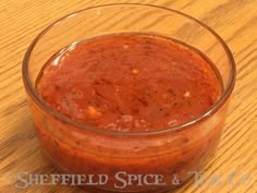 a glass bowl filled with red sauce on top of a wooden table